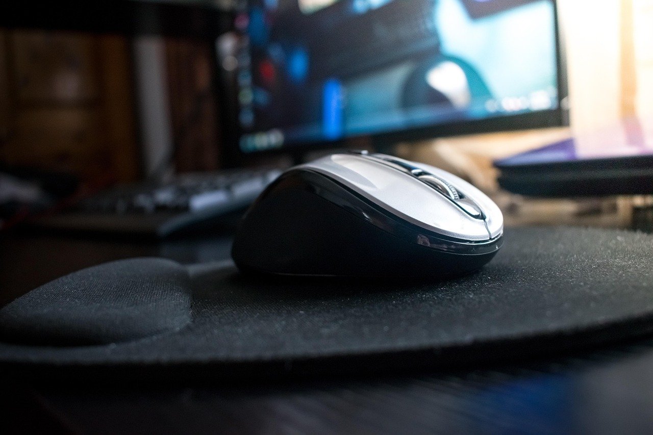 Hand holding a vertical ergonomic mouse in natural handshake position next to keyboard