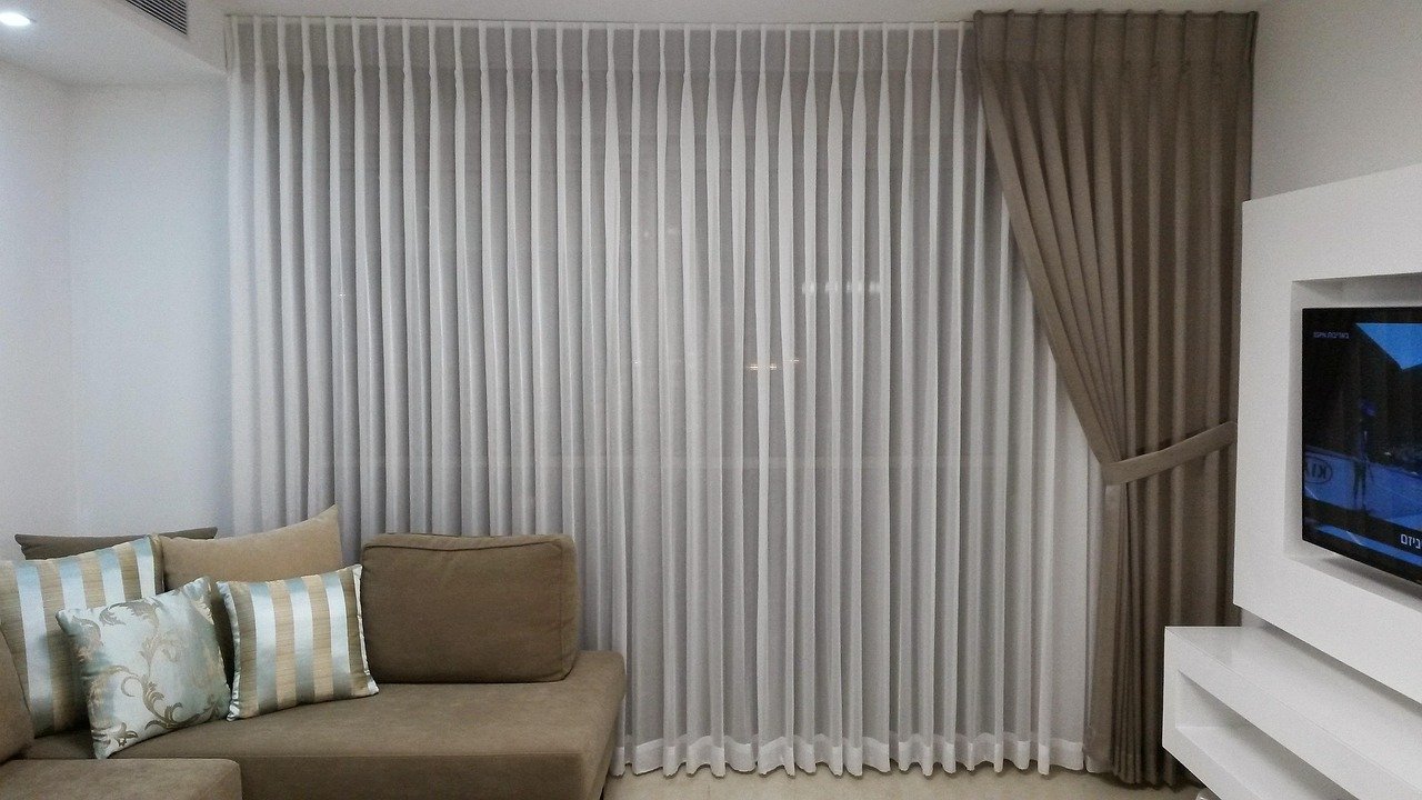 Sala de estar com um par de cortinas longas até o chão em tecido estampado zigue-zague colorido, moldura de janela branca, piso de madeira e um sofá neutro contrastando com a estampa