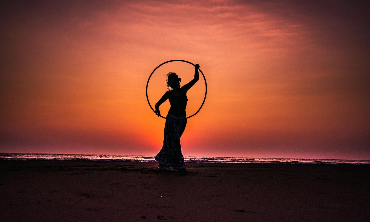 aro de hula hoop com peso (weighted fitness hoop) apoiado contra a parede de um quarto ou sala, ao lado de um tapete de yoga enrolado, ambiente claro e organizado