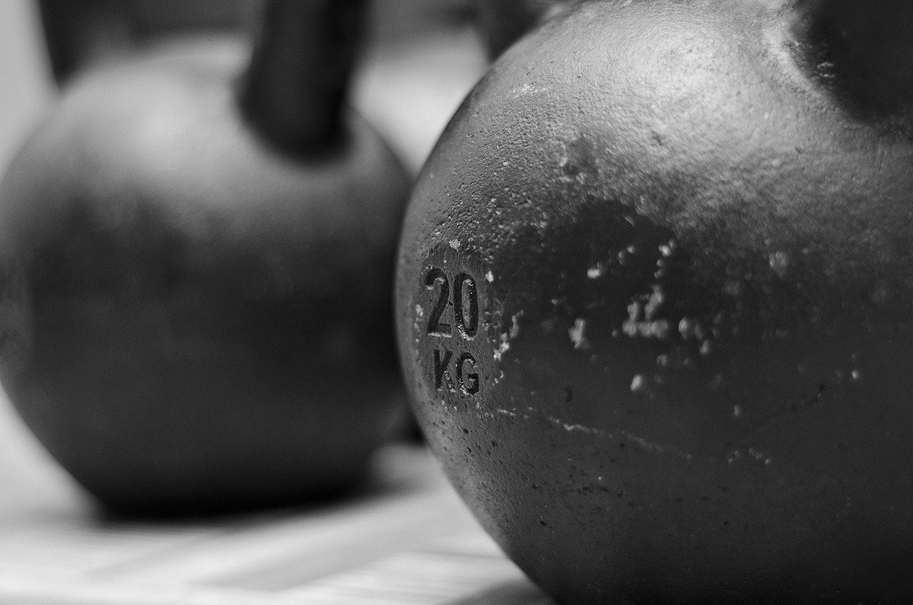 kettlebell revestido de vinil em tom neutro (preto fosco ou terracota), apoiado no chão ao lado de um tapete de exercício texturizado, estilo esteticamente cuidado