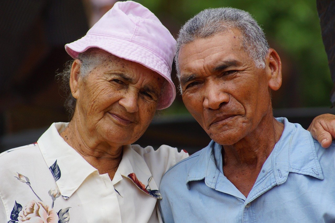 Older couple relaxing on the porch of a large home, conveying comfort and rootedness