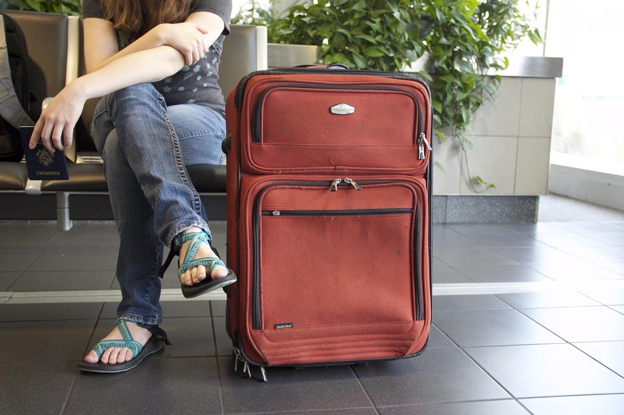 copo de café preso em um suporte/cup caddy clipado na alça de uma mala de rodinhas em um terminal de aeroporto