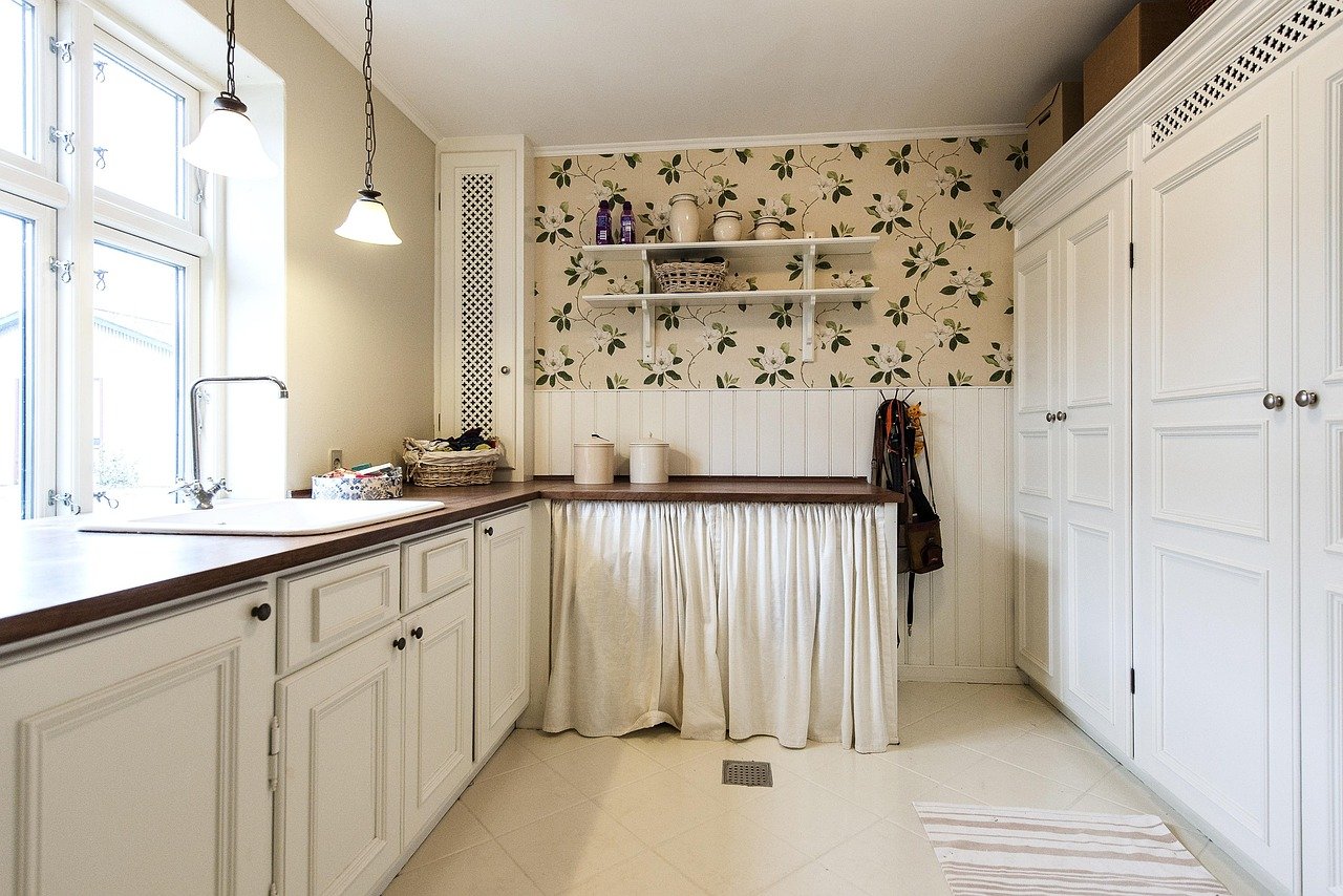 quarto infantil de transição com berço convertido em cama de criança pequena, prateleiras embutidas organizadas com cestos, parede pintada em verde-sálvia fosco e almofada bordada com nome discreto no canto