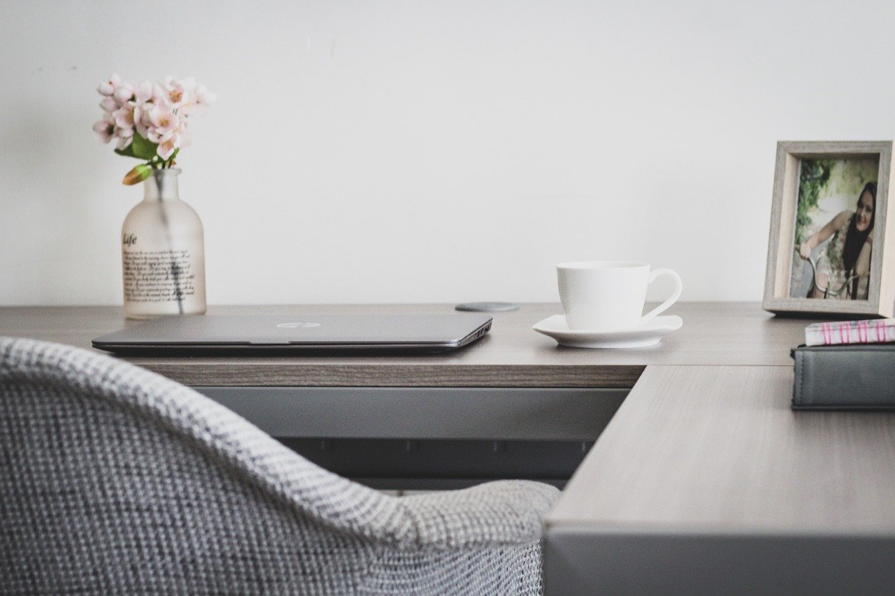 cômodo pequeno transformado em home office e ateliê de hobby, mesa organizada, prateleiras com plantas e objetos pessoais, luz natural entrando pela janela